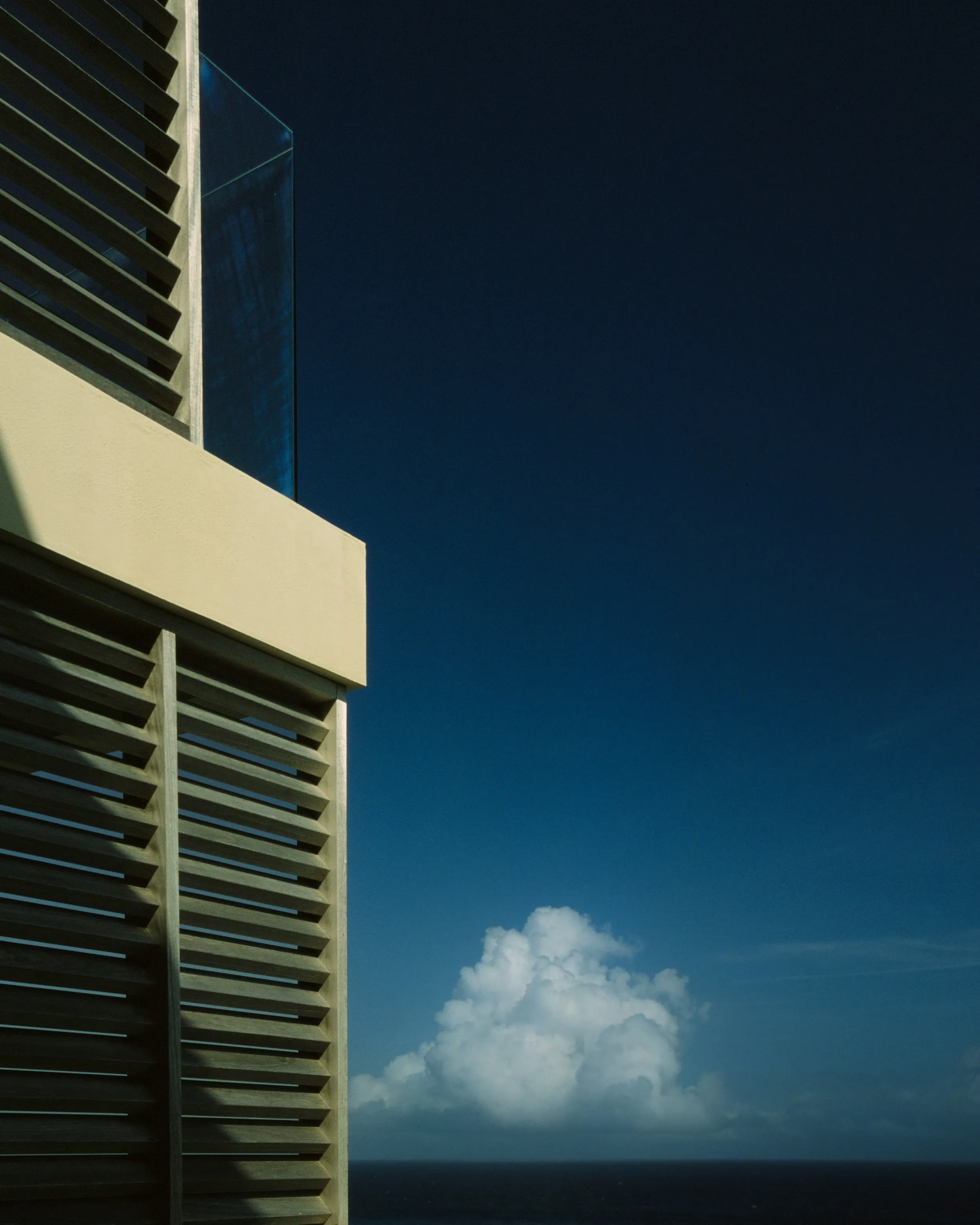 Building corner with shutters and a lone cloud over the sea