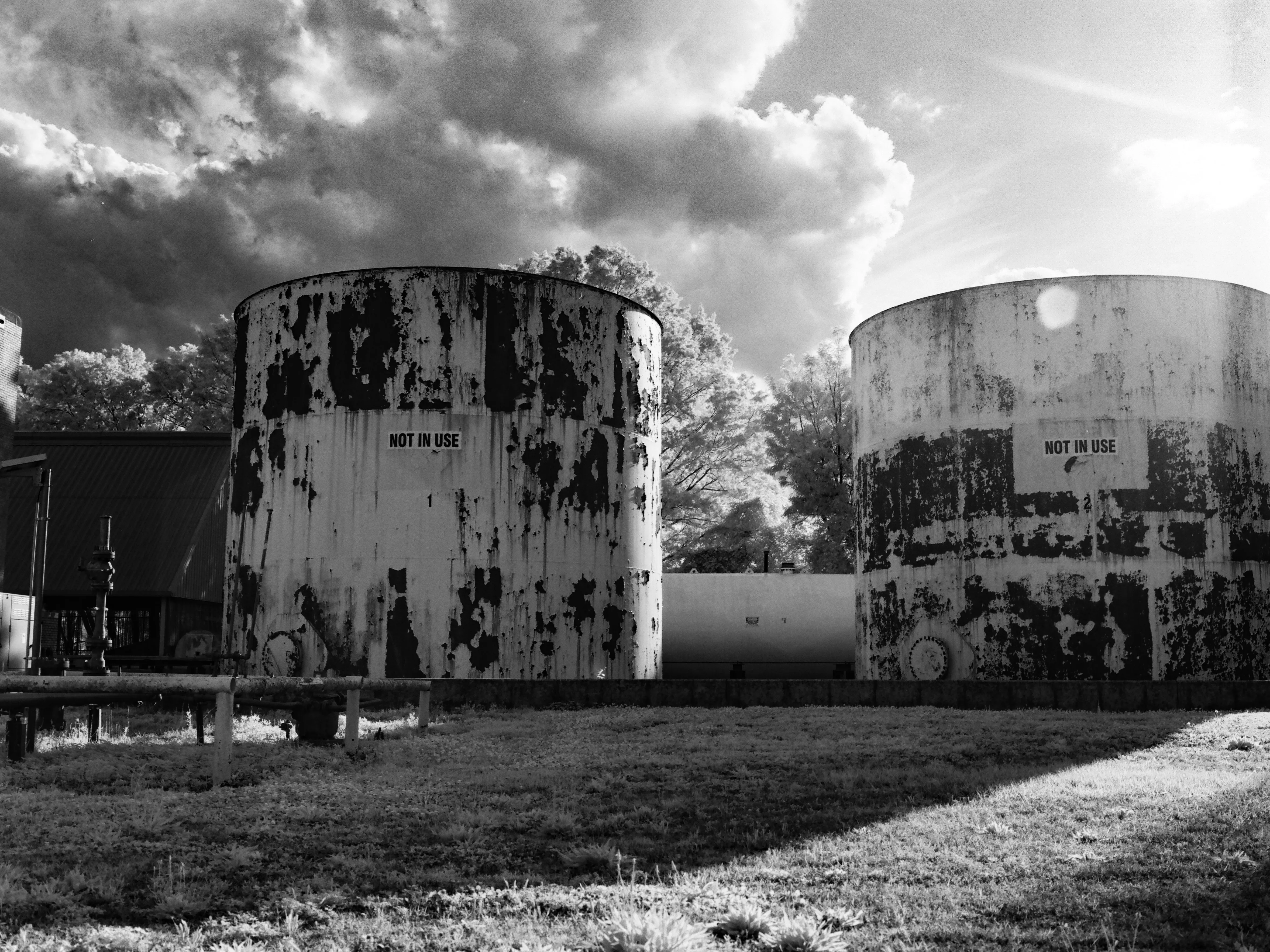 Two weathered industrial storage tanks marked NOT IN USE, dramatic cloud-streaked sky