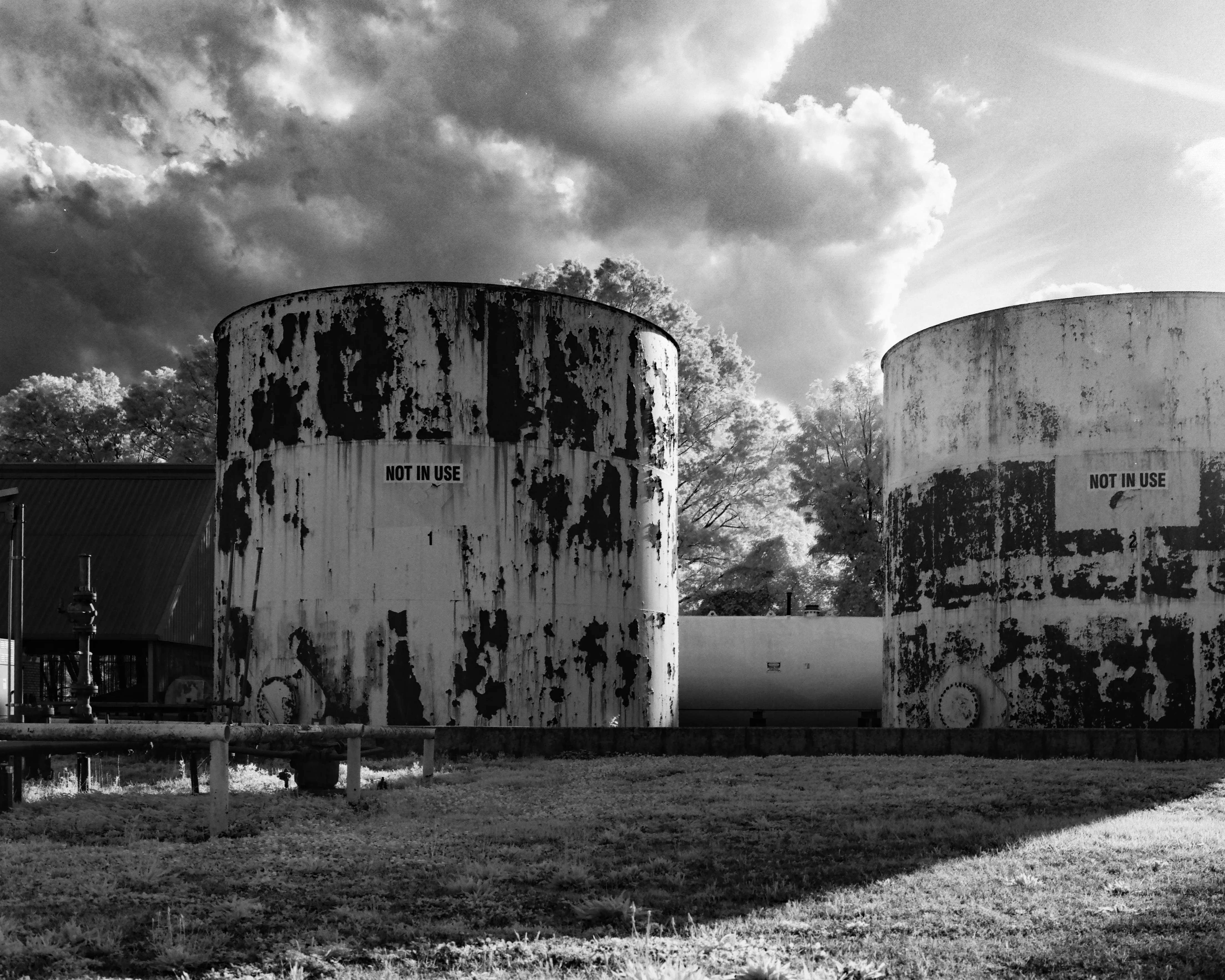 Two weathered storage tanks marked NOT IN USE under a dramatic sky, black and white
