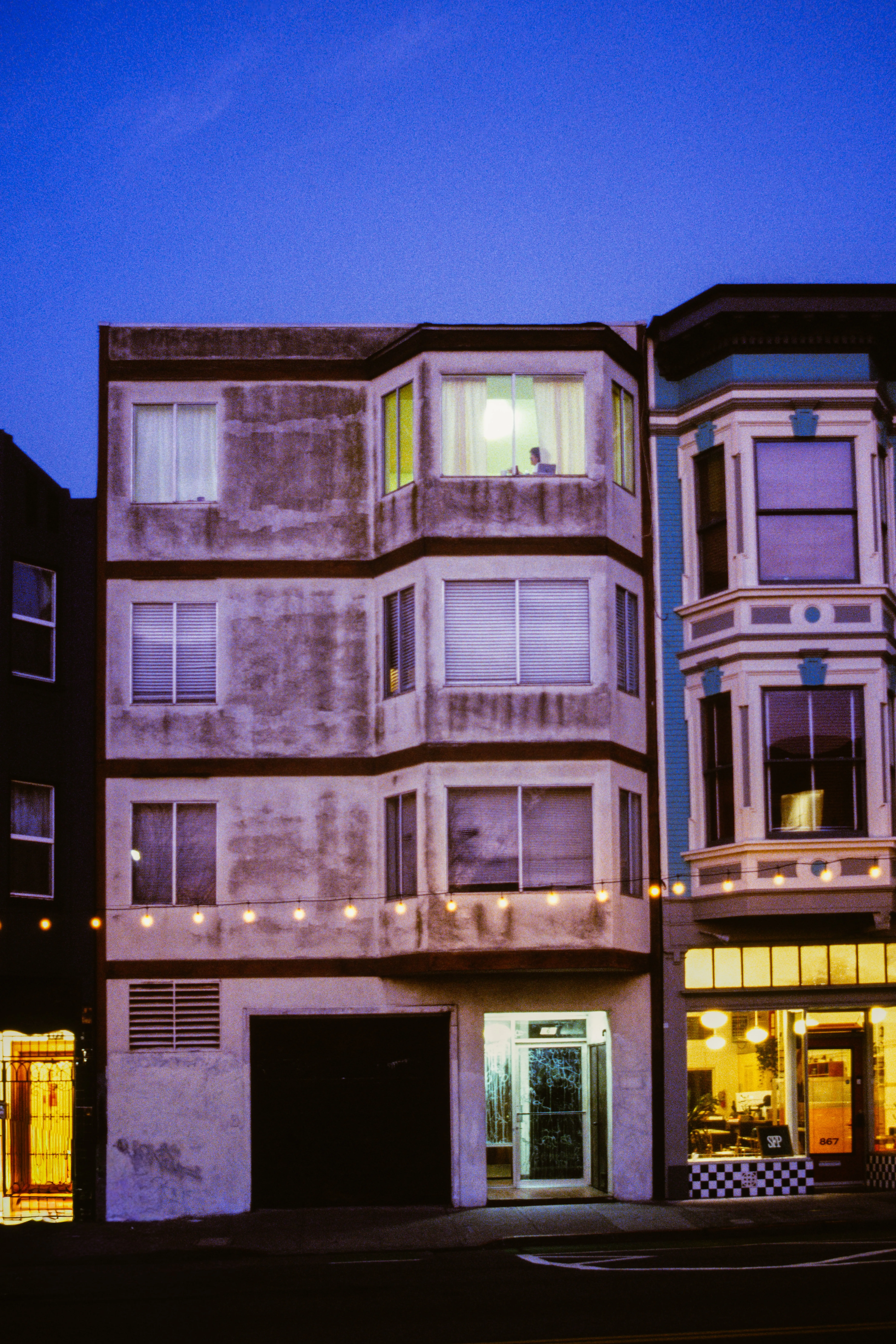 Apartment building at blue hour, single lit upstairs window