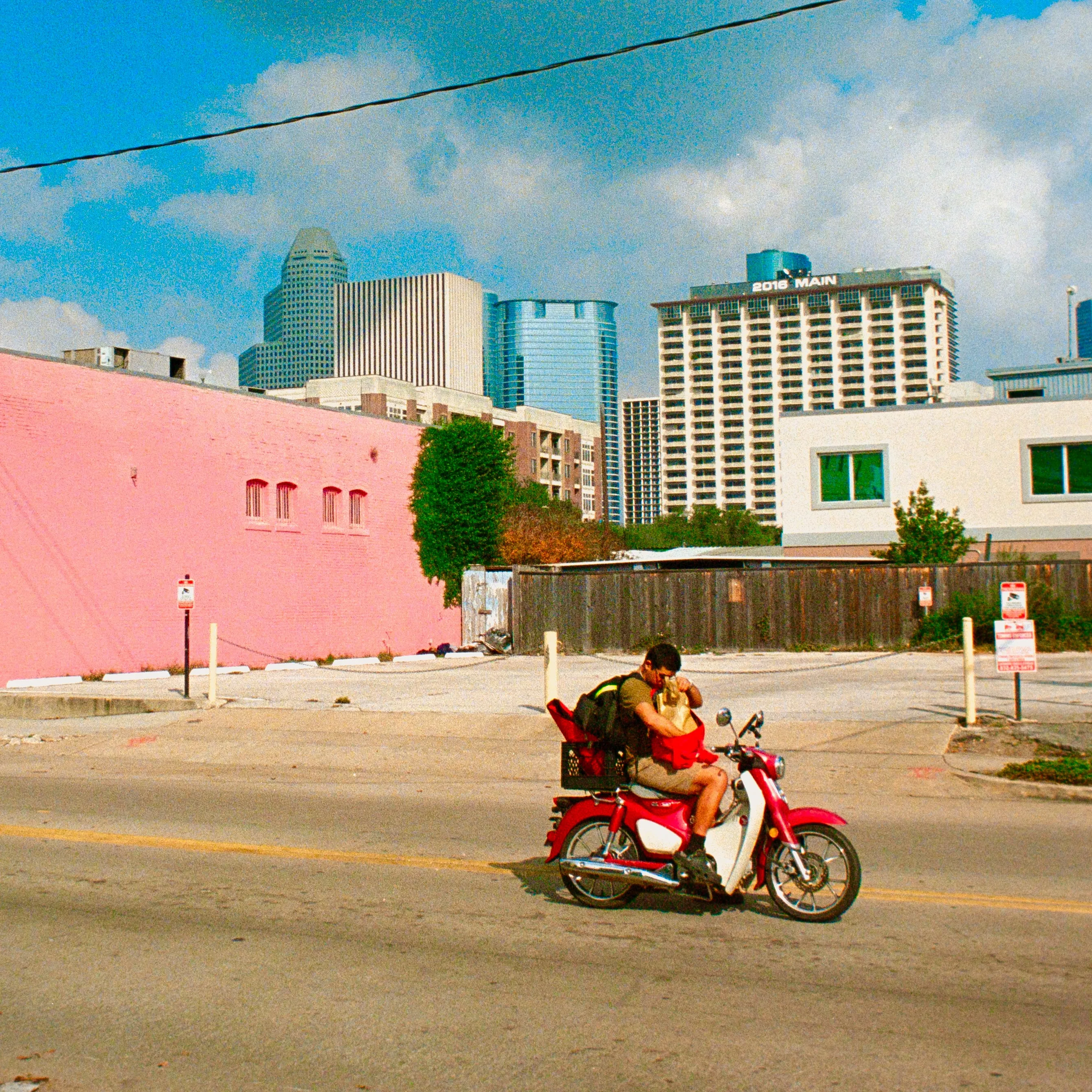 Couple on a red scooter against a pink wall, Houston skyline behind