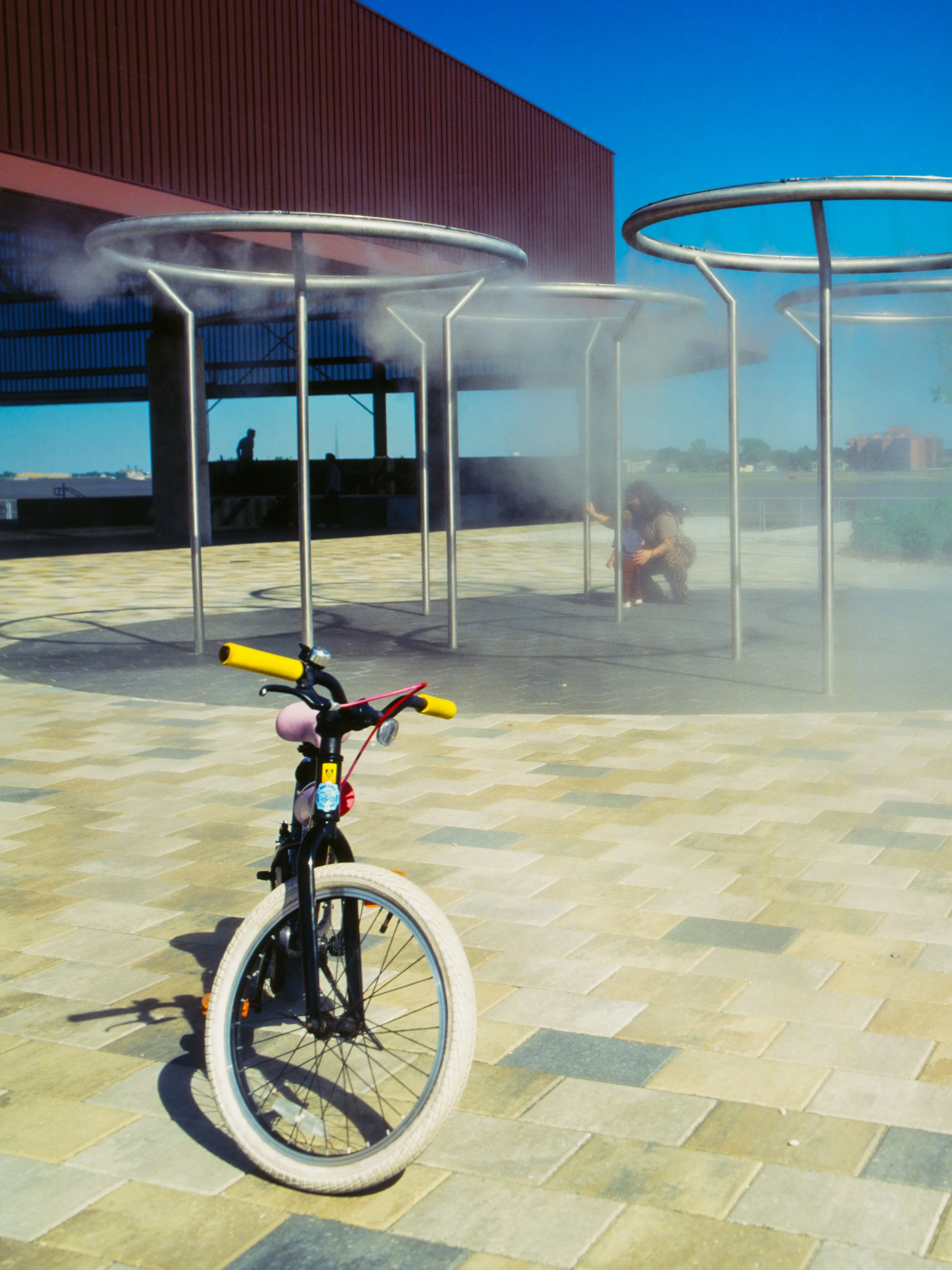 Cooling-mist canopies with figure crouched in the steam, parked bicycle in foreground (recropped)