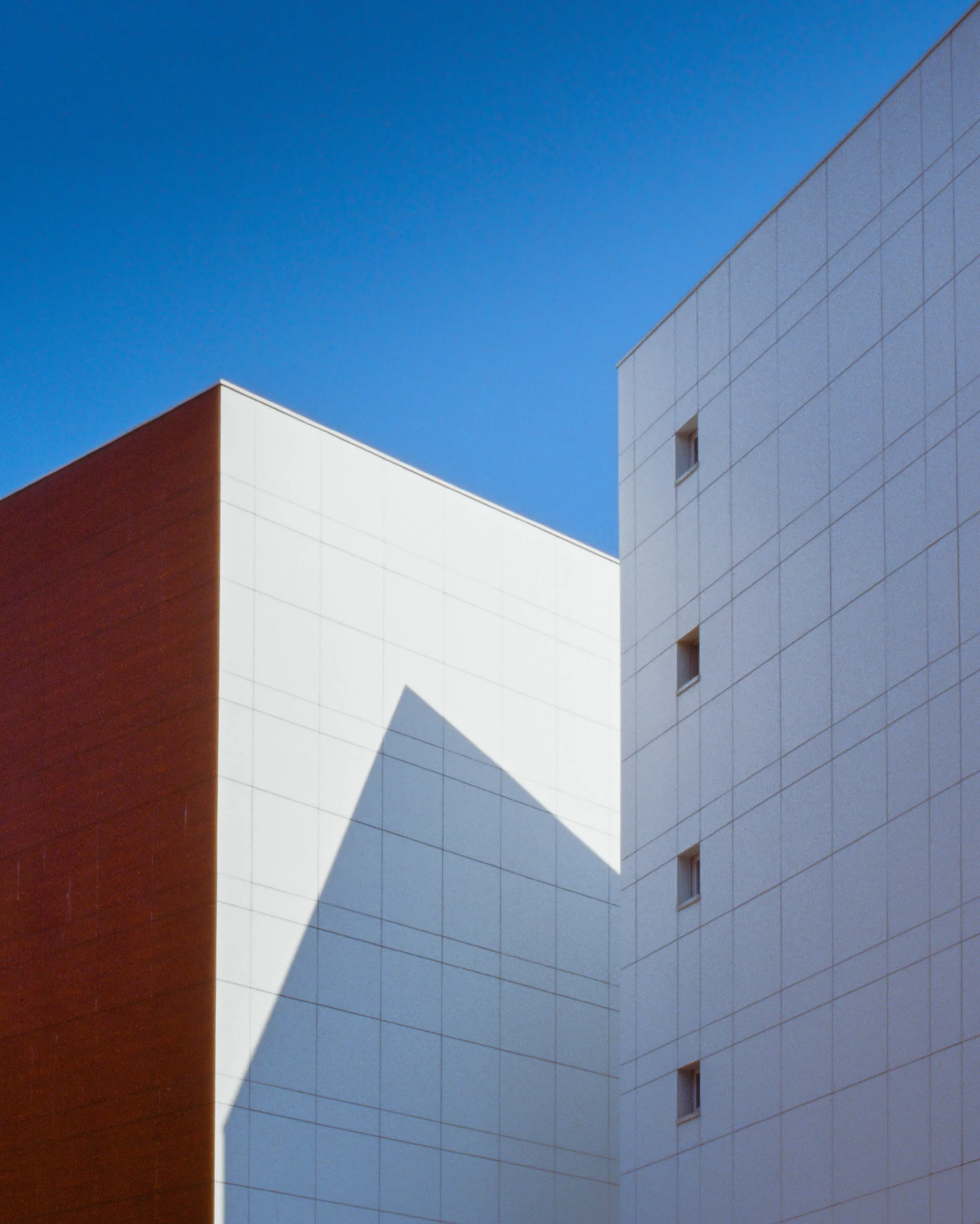 Red and white building corners with a hard triangular shadow, cloudless blue sky