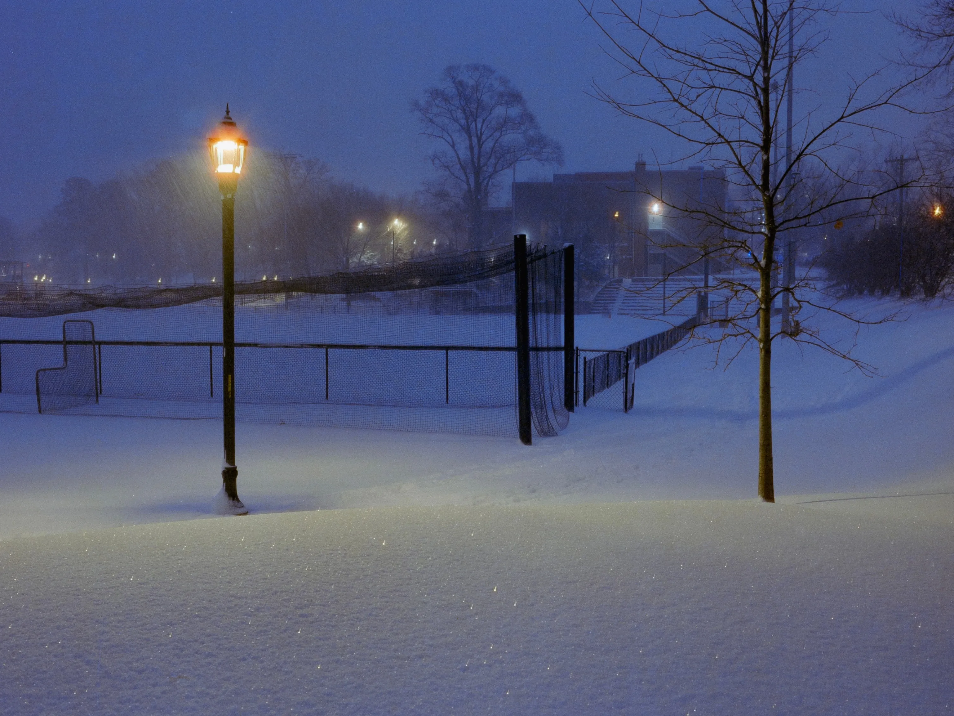 Tennis court fence and lamppost in snow