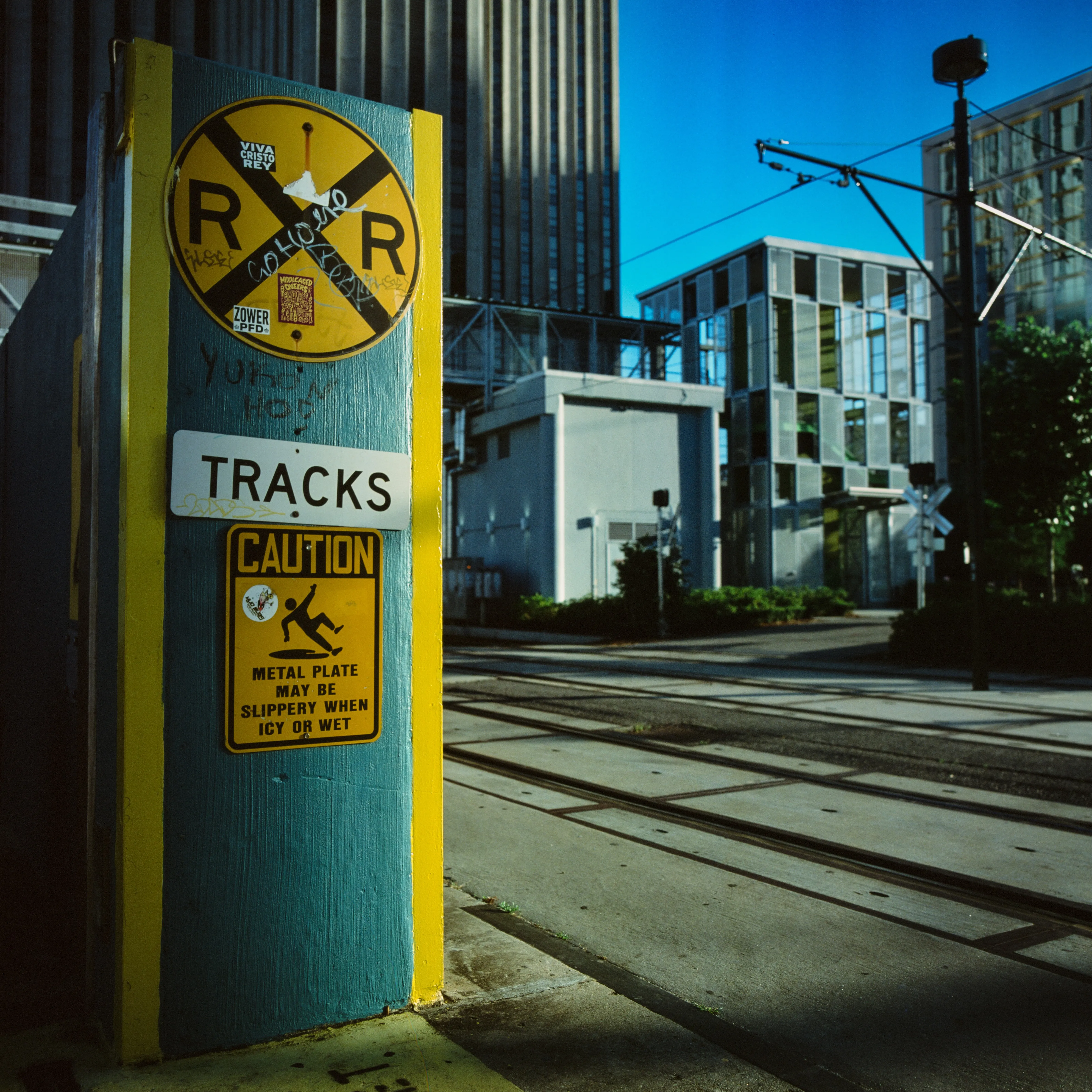 Painted RR crossing post with caution signage, streetcar tracks leading to modern facade, New Orleans