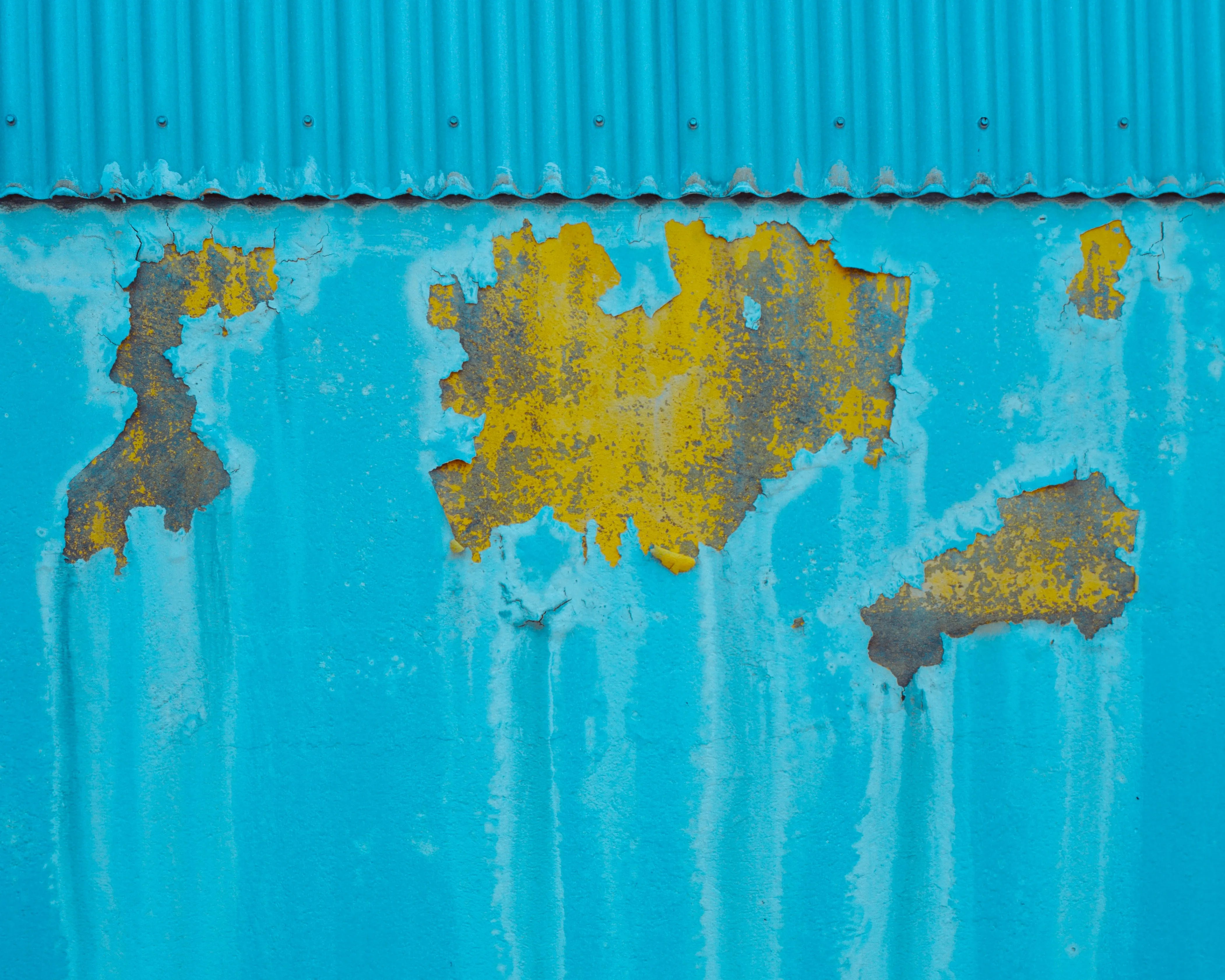 Turquoise corrugated wall with peeling yellow paint scars